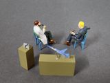 two figurines of men sitting in chairs and one is holding a phone