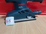 une ponceuse orbitale Bosch posée sur une table en bois, à côté d'une boîte rouge