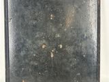 an old black metal plate with rust on it sitting on a white surface