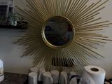 une photo d'un miroir doré en forme de soleil accroché au mur, au-dessus de tasses à café