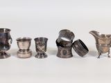five silver cups and a pitcher on a white surface