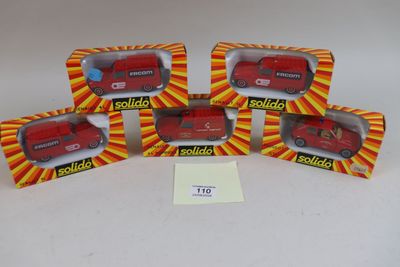 quatre camions rouges miniatures se trouvent dans une boîte posée sur une surface blanche