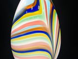 un œuf en verre aux couleurs vives sur fond noir, avec un fil métallique au premier plan