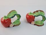 two red apples with green leaves on them on a white surface
