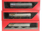 trois boîtes contenant des wagons de train miniature, posées sur une surface blanche