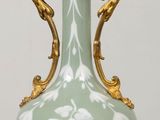 a green vase on a table with a gold base