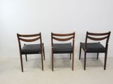 three wooden chairs with black leather seats against a white wall