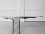 une table en verre transparent avec un piètement en métal, placée au milieu d'une pièce