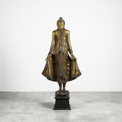 une statue en bronze représentant un Bouddha debout sur un socle