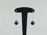 une paire de boucles d'oreilles ornées de perles violettes, suspendues à un support noir