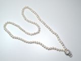 un collier de perles blanches muni d'un fermoir en argent, posé sur une table blanche
