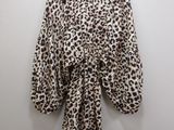 a leopard print top hangs on a hanger against a white wall