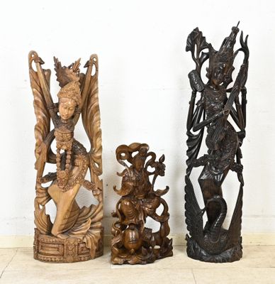 trois statues en bois assises les unes à côté des autres sur le sol