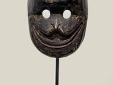 a wooden mask on a black stand with a white background