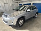 La voiture argentée est garée dans un garage dont la porte est bleue.
