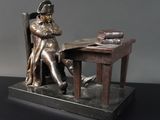 une statue représentant un homme assis à un bureau, un livre à la main