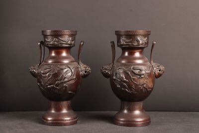 une paire de vases anciens en bronze posés sur une table, sur fond gris