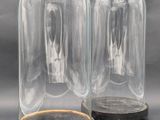 pair of clear glass cloches with wooden base on grey background