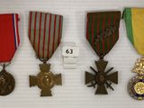trois médailles et une croix sont exposées sur un socle blanc