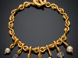 a gold bracelet with pearls and charms on a black background