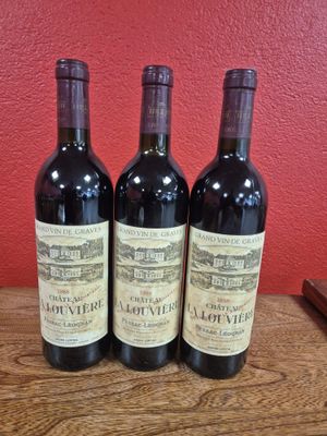 Trois bouteilles de vin sont posées sur une table en bois devant un mur rouge.