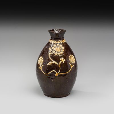 vase marron et doré orné de fleurs et de feuilles sur fond gris