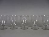 six empty wine glasses lined up in a row on a white surface