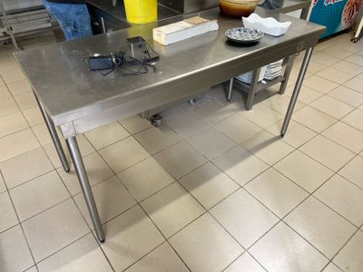 une table en acier inoxydable dans la cuisine, sur laquelle se trouve un saladier rempli de nourriture