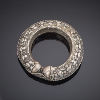 an antique silver bangle on a black surface with a black background
