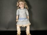une poupée à l'ancienne, vêtue d'une robe à rayures bleues et blanches et de chaussures marron