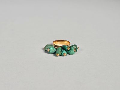 un gros plan d'une bague en or sertie de pierres vertes sur un fond blanc