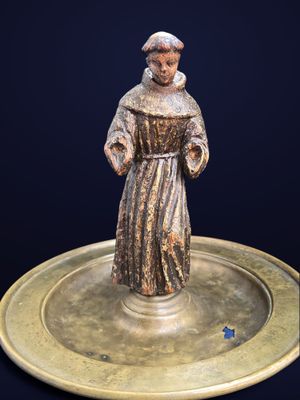 figurine en bronze représentant un moine, posée sur une plaque en laiton sur fond noir