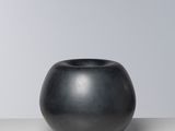 un vase noir posé sur une table près d'un mur blanc