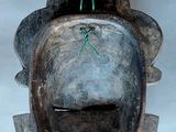 a wooden mask hanging on the wall with a green string