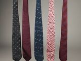 four different colored ties hanging from a line against a gray background