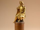 bronze statue of a woman sitting on a pedestal on a beige background