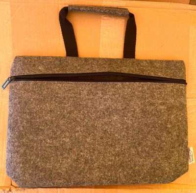 un sac d'ordinateur portable gris avec des fermetures éclair noires, posé sur une boîte en carton