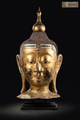 une tête de Bouddha dorée posée sur un socle, sur fond noir