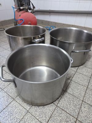 trois casseroles en métal posées sur le carrelage d'une cuisine
