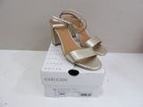 the box is white and has a pair of metallic sandals on it