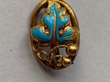 broche en or et turquoise ornée de feuilles sur un fond blanc