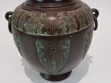 un vase marron orné de motifs verts sur un fond blanc