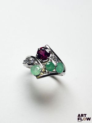 un gros plan d'une bague posée sur une surface blanche, ornée de pierres vertes et rouges