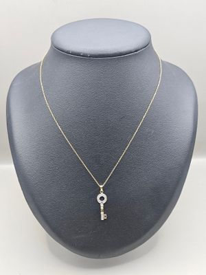 a gold necklace with a diamond key on a mannequin neck