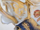 a close up of a blue and gold vase on a white surface