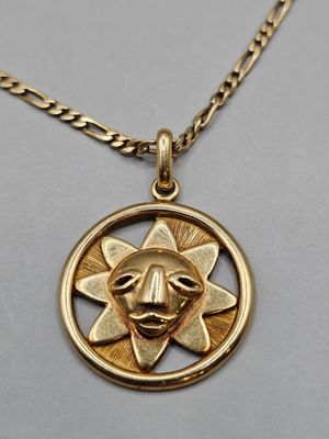 a close up of a gold necklace with a sun in the middle