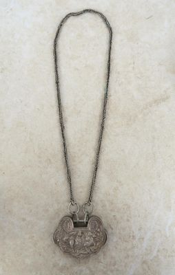 un vieux collier en argent orné d'un oiseau, posé sur un fond blanc