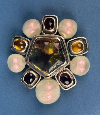 silver and glass broochle with multi colored stones on a blue surface