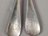 pair of silver spoons with initials on them sitting on a table
