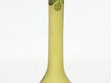 a green vase with leaves on it on a white surface